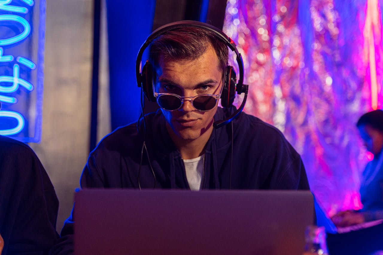 contact-img Focused man in headphones and sunglasses uses laptop in vibrant studio setting.