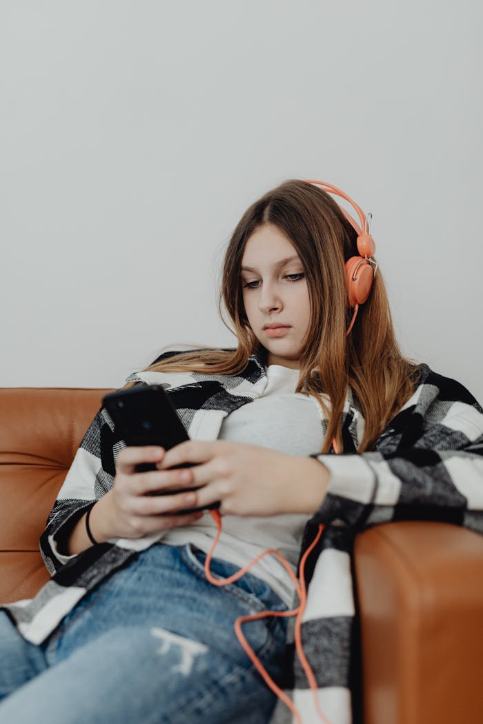 gallery-1 Teenager in headphones relaxing on a sofa, listening to music using a smartphone.