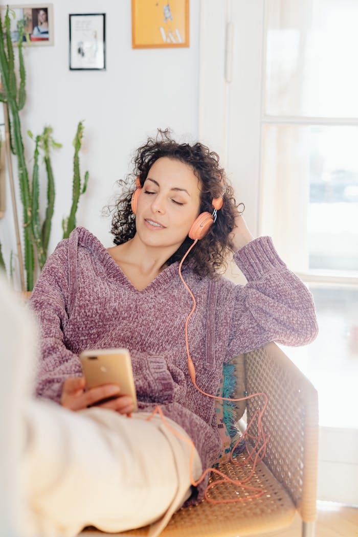 why-choose-us Woman sitting indoors enjoying music with headphones and smartphone.