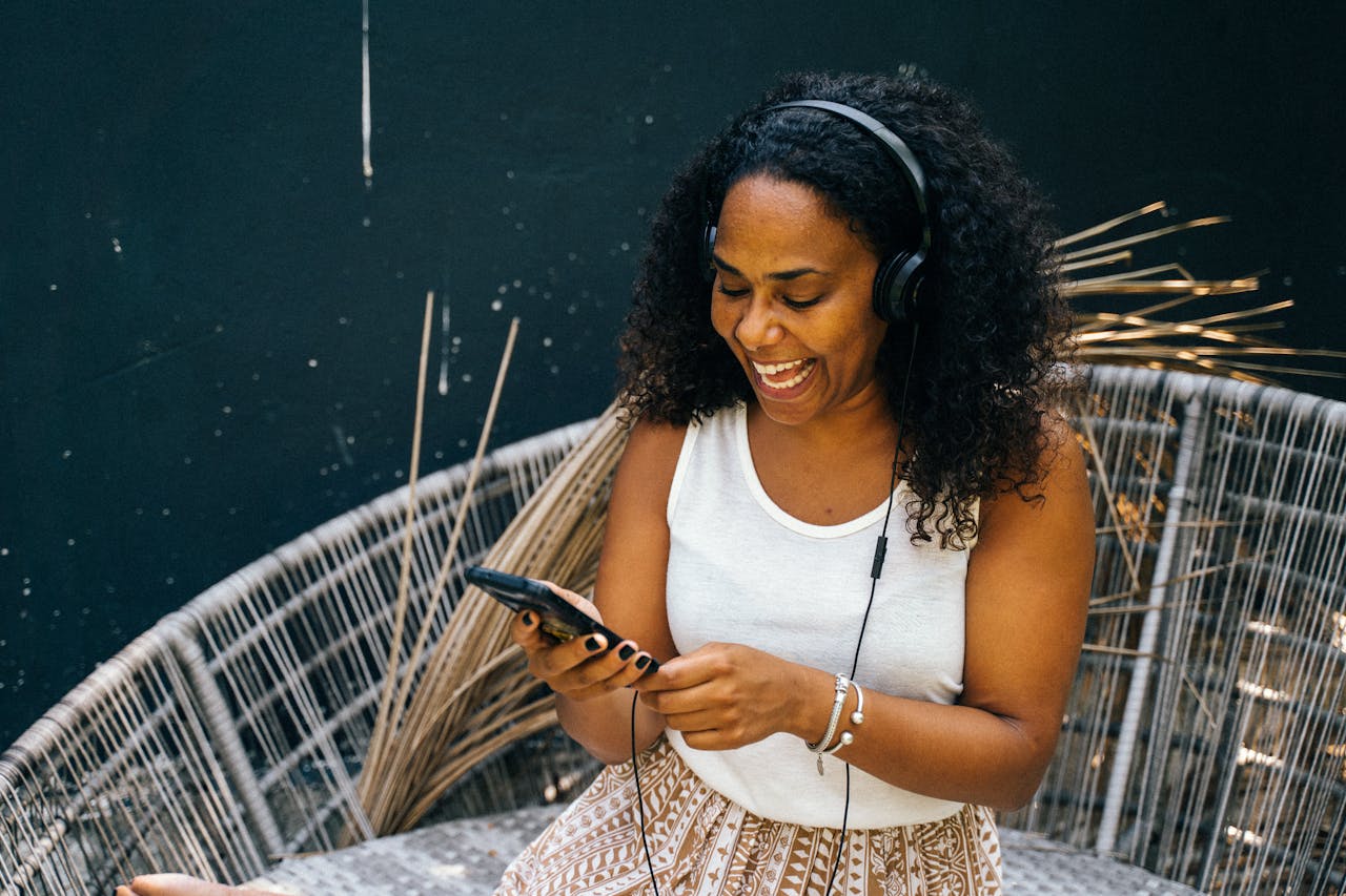 our-services-1 A joyful woman sitting outdoors, listening to music on headphones and using her phone.