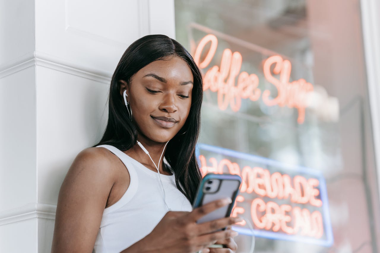 about-01 Smiling woman with earphones using smartphone outside a coffee shop.